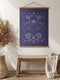 A symmetrical wall tapestry in monochromatic navy blue featuring a detailed scarab beetle surrounded by flowers and botanical elements, mounted on a wooden dowel with natural twine.